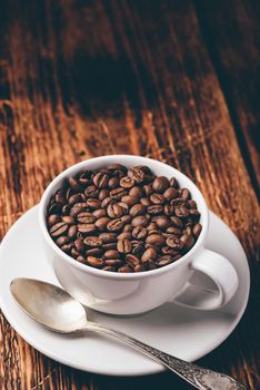 Cup full of roasted coffee beans on saucer over wooden table