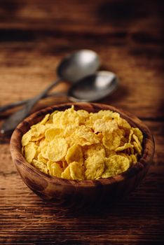 Rustic bowl of corn flakes with spoons on a wooden surface