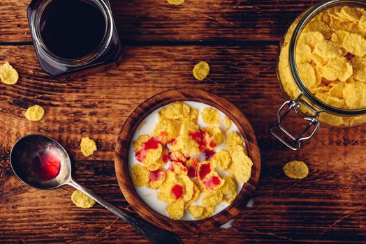 Breakfast with corn flakes, milk and berry syrup. View from above