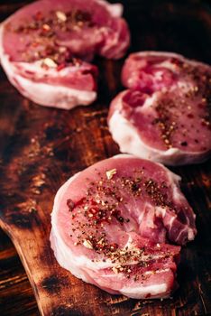 Raw pork loin steaks with different spices on rustic cutting board