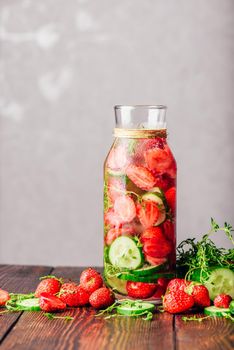 Bottle of Infused Water with Fresh Strawberry, Sliced Cucumber and Springs of Thyme. Ingredients Scattered on Wooden Table. Copy Space and Vertical Orientation.