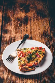 Slice of vegetable frittata with broccoli, red bell pepper and red onion on white plate