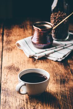 Cup of turkish coffee with copper cezve and jar of roasted coffee beans on wooden table
