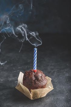Birthday chocolate muffin with smoking candle on dark concrete background