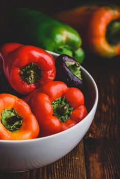 Multicolored fresh bell peppers in bowl over wooden background