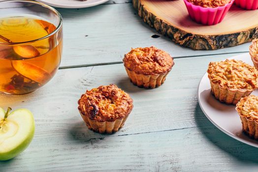 Healthy Breakfast. Cooked oatmeal muffins with apple and cup of green tea over light wooden background.