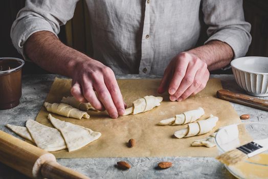 Homemade croissant preparing. Baker rolls the puff pastry stuffed with chopped almonds and hazelnut spread