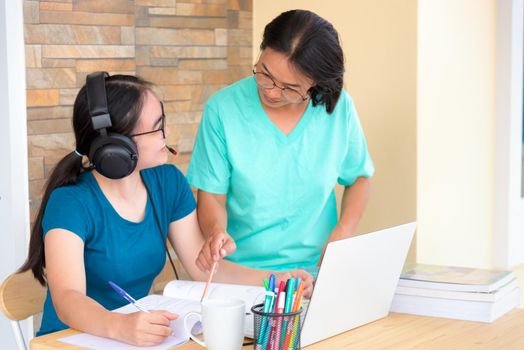 Happy two Asian woman mother is a teacher advice instruction to her daughter teenage girl student online study from school using a laptop computer education from university class learning from home