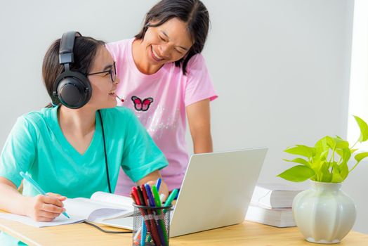 Happy family two Asian woman mother parent is a teacher advice instruction daughter teenage girl student online study from school use a laptop computer education from university class learning at home