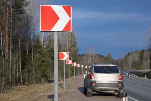 Close-up of a road sign and a car in the background, parked on the side of the road.