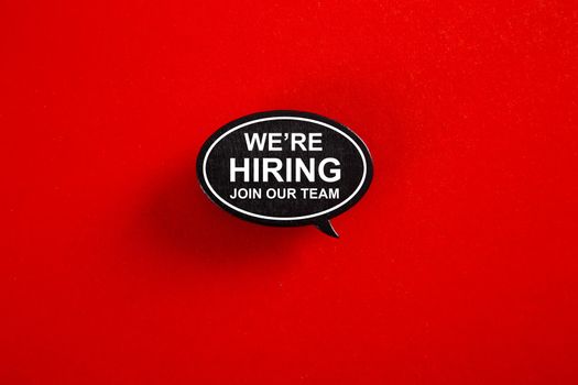 WE'RE HIRING in speech bubble isolated on red paper background with drop shadow.
