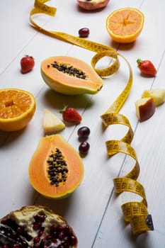 the concept for the diet: some fruits and a tape measure on a white wooden table