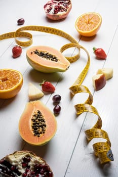 the concept for the diet: some fruits and a tape measure on a white wooden table