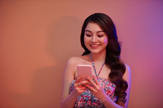 Reading new messages. Beautiful young Asian woman holding mobile phone while standing