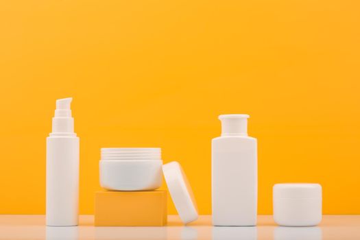 Set of white plastic cosmetic bottles with products for skin care against bright orange background. Concept of cosmetic with citrus extracts