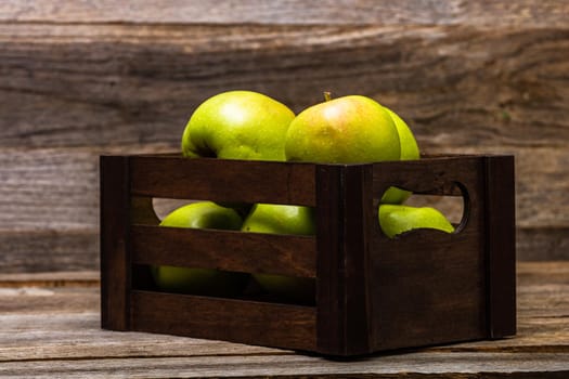 Wooden crate with ripe green apples on wooden table.