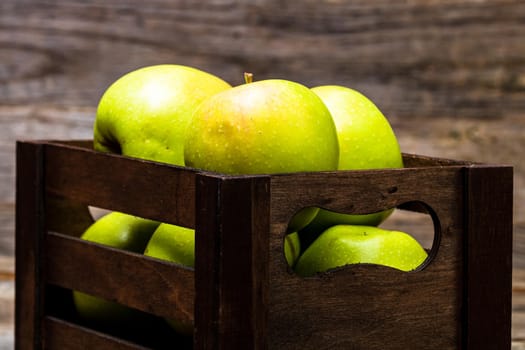 Wooden crate with ripe green apples on wooden table.