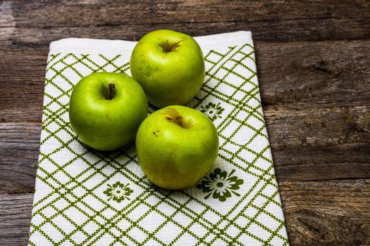 Ripe green apples on a rustic napkin on wooden table.