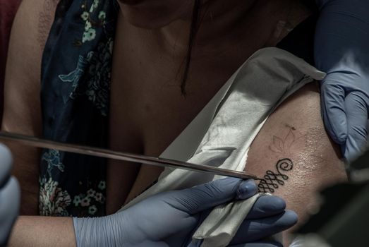 Bangkok, Thailand - 25 Aug 2019 : Tattooing Thai style concepts. Tattoo artist creating a tattoo on a girl's arm with a pointed metal.