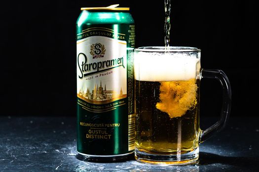 Can of Staropramen beer and beer glass on dark background. Illustrative editorial photo shot in Bucharest, Romania, 2021