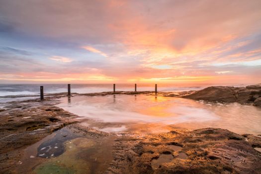 Beautiful sunrise over a natural ocean rock pool near Sydney Australia.  Focus to foreground rocks with lovely pastel sky and soft flowy waves.
