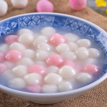 Close up of red and white tangyuan (tang yuan, glutinous rice dumpling balls) in blue bowl on wooden background for Winter solstice festival food.