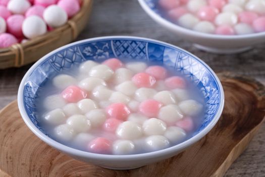 Close up of red and white tangyuan (tang yuan, glutinous rice dumpling balls) in blue bowl on wooden background for Winter solstice festival food.