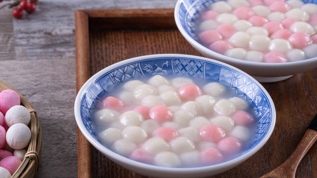 Close up of red and white tangyuan (tang yuan, glutinous rice dumpling balls) in blue bowl on wooden background for Winter solstice festival food.
