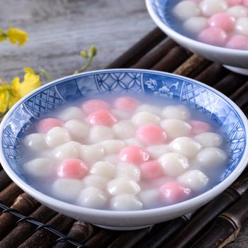 Close up of red and white tangyuan (tang yuan, glutinous rice dumpling balls) in blue bowl on wooden background for Winter solstice festival food.