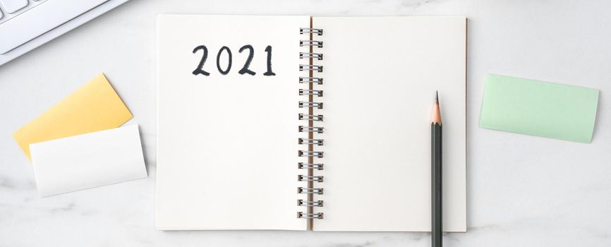 Top view of office table desk 2021 Goal work concept with keyboard, notebook, pencil, eyeglasses and coffee on bright marble white background.