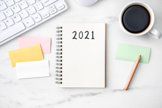 Top view of office table desk 2021 Goal work concept with keyboard, notebook, pencil, eyeglasses and coffee on bright marble white background.