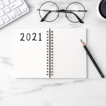 Top view of office table desk 2021 Goal work concept with keyboard, notebook, pencil, eyeglasses and coffee on bright marble white background.
