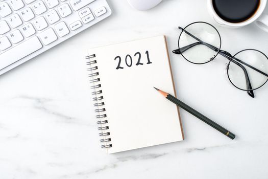 Top view of office table desk 2021 Goal work concept with keyboard, notebook, pencil, eyeglasses and coffee on bright marble white background.