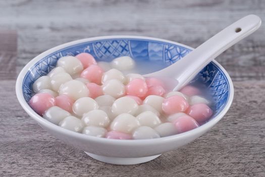 Close up of red and white tangyuan (tang yuan, glutinous rice dumpling balls) in blue bowl on wooden background for Winter solstice festival food.