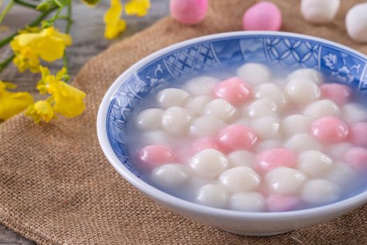 Close up of red and white tangyuan (tang yuan, glutinous rice dumpling balls) in blue bowl on wooden background for Winter solstice festival food.