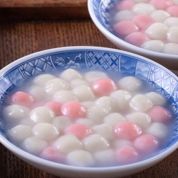 Close up of red and white tangyuan (tang yuan, glutinous rice dumpling balls) in blue bowl on wooden background for Winter solstice festival food.