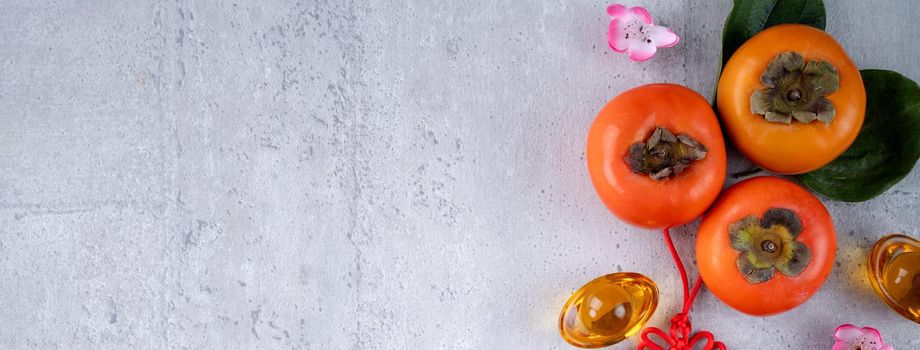 Top view of fresh sweet persimmons kaki with leaves on gray table background for Chinese lunar new year fruit design concept, the word means spring is coming.