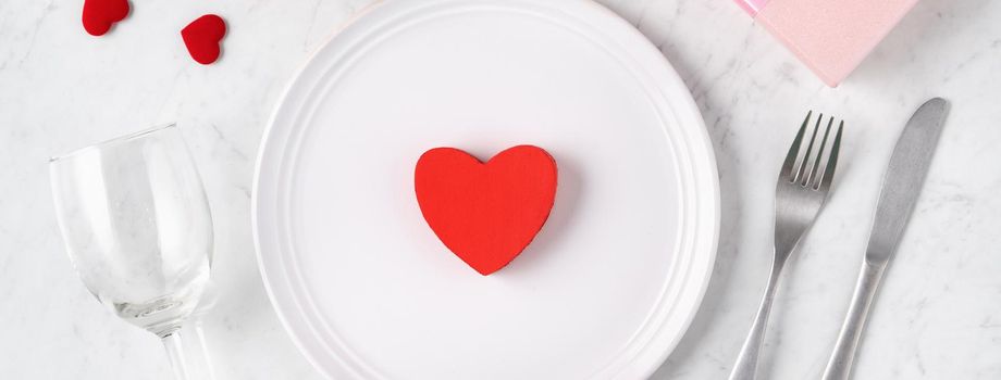 Empty white plate with tableware, ribbon, gift and roses for Valentine's Day special holiday dating meal concept.