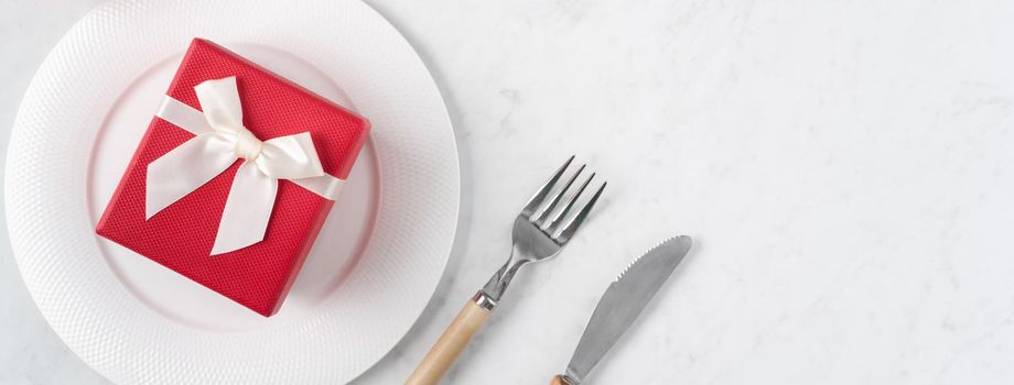 Empty white plate with tableware, ribbon, gift and roses for Valentine's Day special holiday dating meal concept.