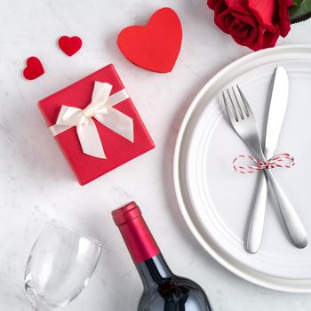 Empty white plate with tableware, ribbon, gift and roses for Valentine's Day special holiday dating meal concept.