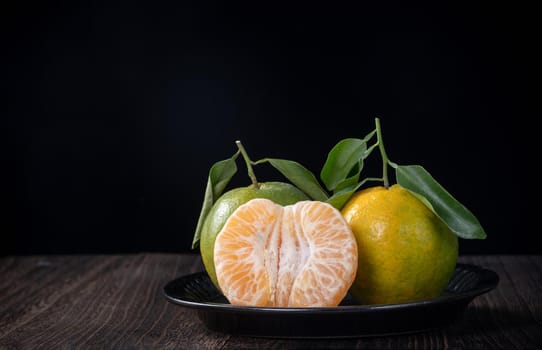 Fresh green tangerine mandarin orange with fresh leaves on dark wooden table background harvest concept.