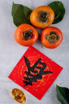 Top view of fresh sweet persimmons kaki with leaves on gray table background for Chinese lunar new year fruit design concept, the word means spring is coming.