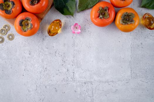 Top view of fresh sweet persimmons kaki with leaves on gray table background for Chinese lunar new year fruit design concept, the word means spring is coming.