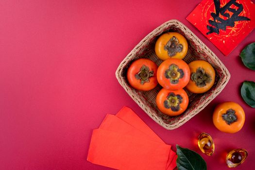 Top view of fresh sweet persimmons kaki with leaves on red table background for Chinese lunar new year fruit design concept, the word means spring is coming.