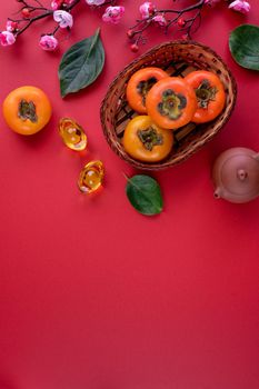 Top view of fresh sweet persimmons kaki with leaves on red table background for Chinese lunar new year fruit design concept, the word means spring is coming.