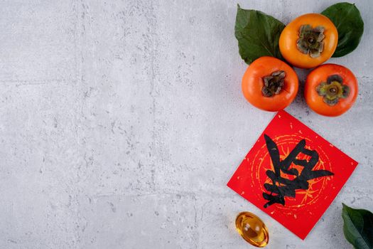 Top view of fresh sweet persimmons kaki with leaves on gray table background for Chinese lunar new year fruit design concept, the word means spring is coming.