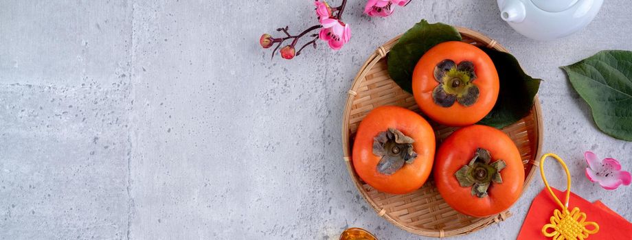 Top view of fresh sweet persimmons kaki with leaves on gray table background for Chinese lunar new year fruit design concept, the word means spring is coming.