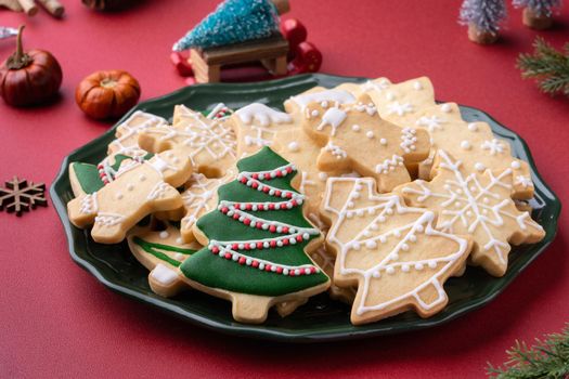 Close up of Christmas decorated sugar cookies in a plate on red table background.