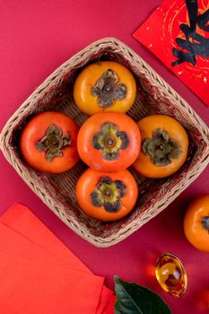 Top view of fresh sweet persimmons kaki with leaves on red table background for Chinese lunar new year fruit design concept, the word means spring is coming.