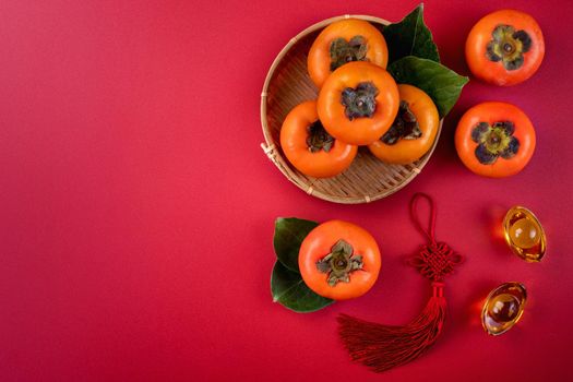 Top view of fresh sweet persimmons kaki with leaves on red table background for Chinese lunar new year fruit design concept, the word means spring is coming.